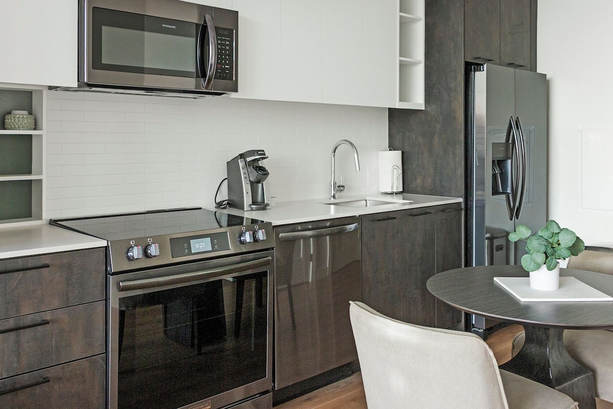 Une cuisine moderne équipée d’un four, d’un micro-ondes et d’un réfrigérateur intégrés. Un coin repas avec une table et des chaises est également disponible.