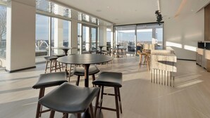 Un espace de restauration moderne avec des tables rondes et des tabourets de bar, de grandes fenêtres offrant une vue sur la ville et un comptoir de bar en marbre.