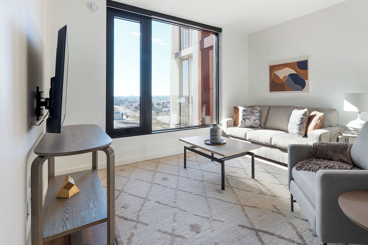 Un salon moderne comprenant un canapé, un fauteuil, une table basse et un téléviseur à écran plat fixé au mur.