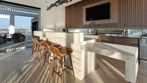 Une cuisine moderne dotée d’un plan de travail en marbre, de tabourets de bar en bois et d’une grande fenêtre donnant sur un paysage urbain.