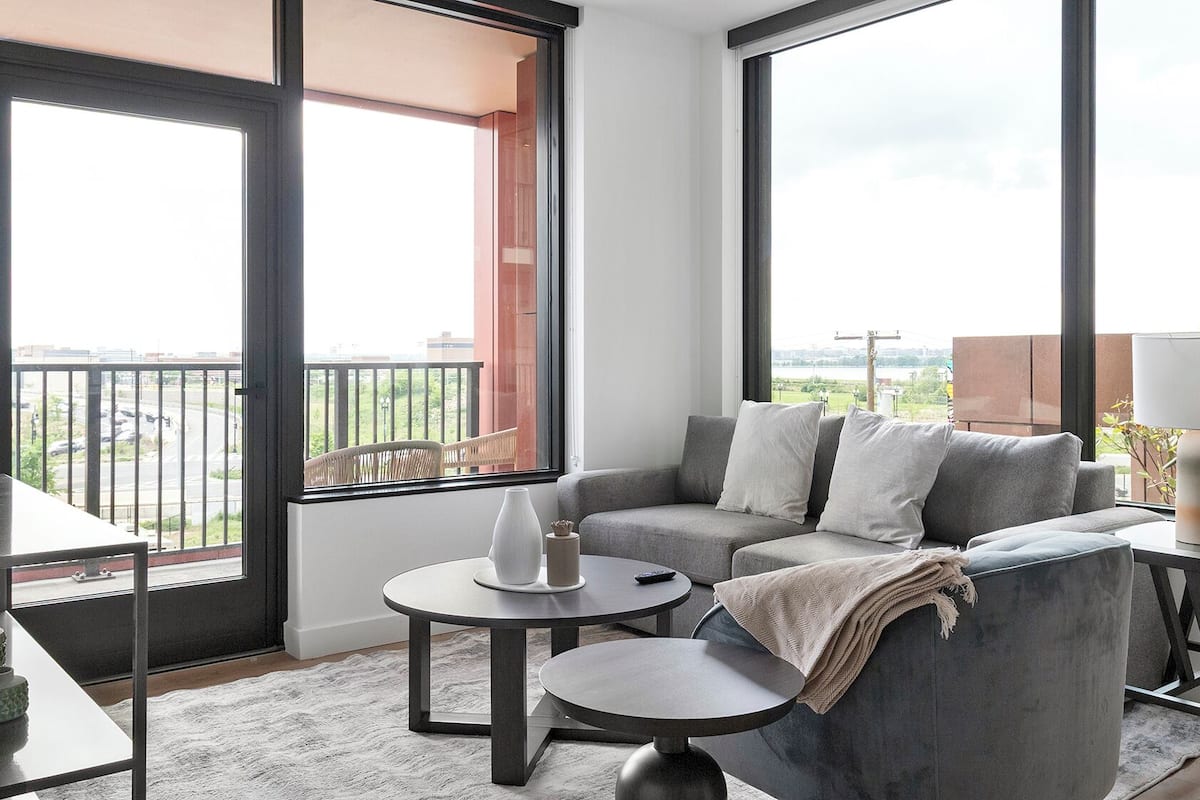 Un salon moderne avec un canapé gris, deux tables rondes et un balcon offrant une vue sur la ville.