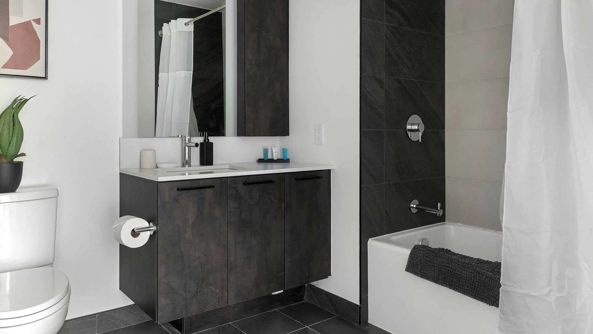 Un baño moderno con tocador de mármol oscuro, lavamanos blanco y bañera.