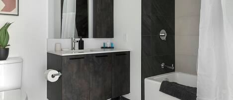 Un baño moderno con tocador de mármol oscuro, lavamanos blanco y bañera.
