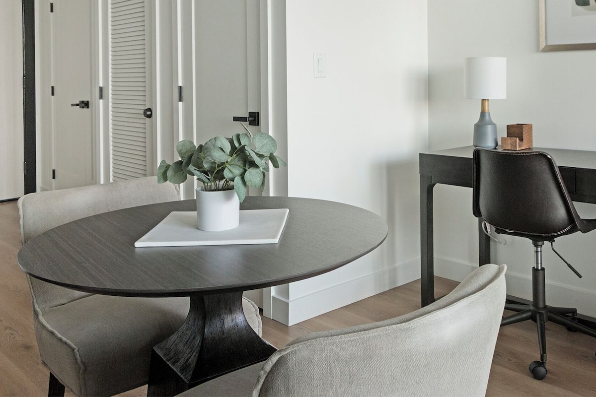 Un espace repas moderne comprenant une table ronde, deux chaises, une plante en pot, un bureau avec une chaise et une lampe.