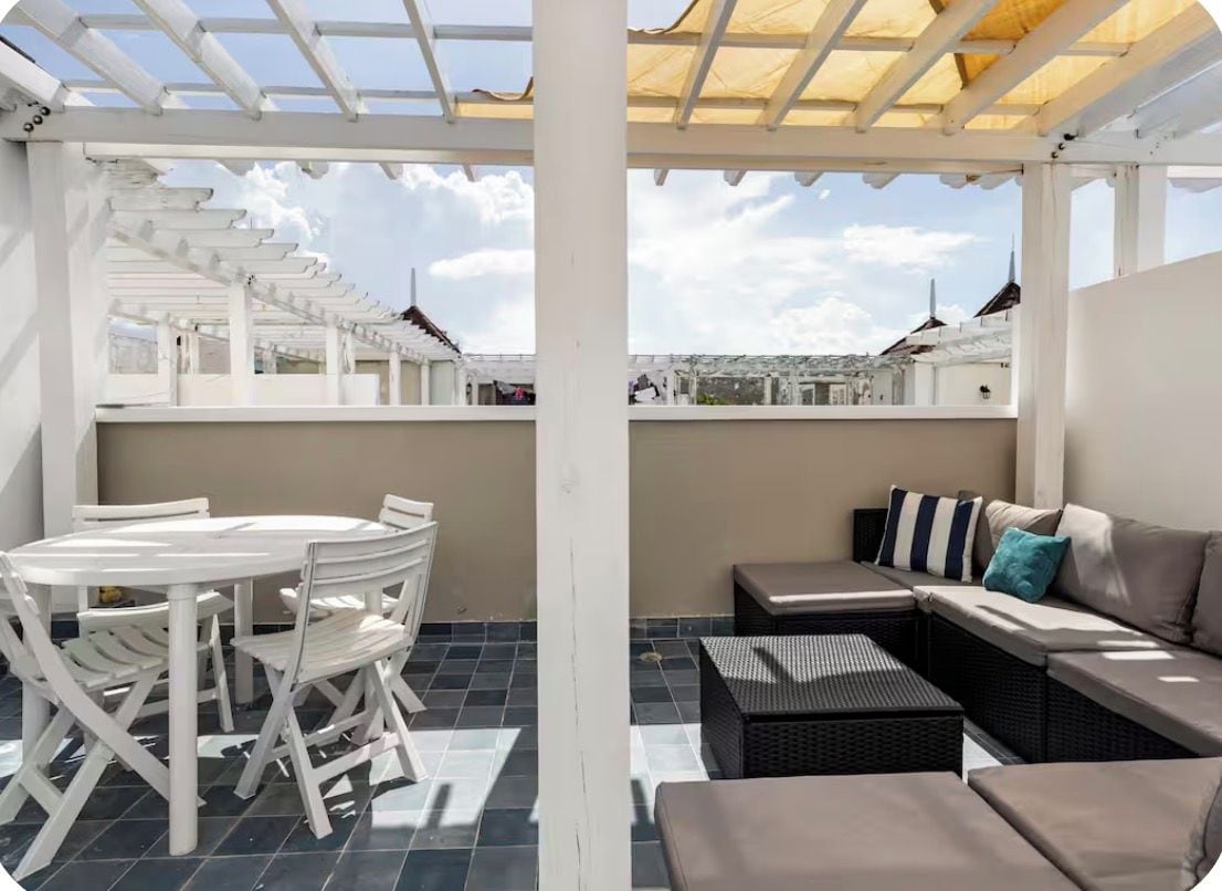 A covered outdoor seating area with a round table and chairs, a sofa, and a view of the cityscape.