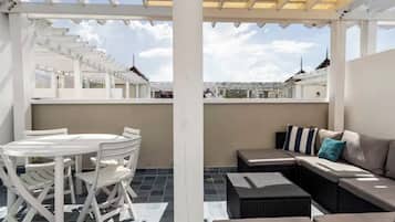 A covered outdoor seating area with a round table and chairs, a sofa, and a view of the cityscape.