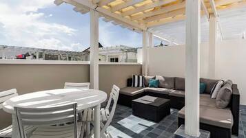 An outdoor patio area with a round table, white chairs, a sofa, and a pergola structure.