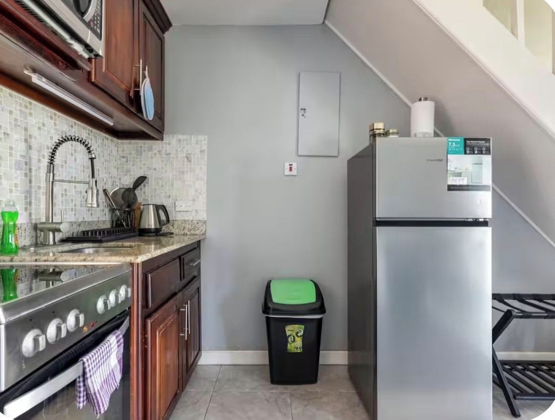 A kitchen with a stainless steel refrigerator, a stove, and a trash bin.