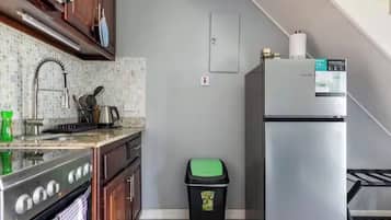 A kitchen with a stainless steel refrigerator, a stove, and a trash bin.
