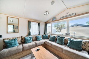 A cozy living room with a sectional sofa, a wooden coffee table, and a large window offering a view of the outside. - 3 Bed-Sleeps 8-Pet Friendly-Parking-Sea View (Exmouth)