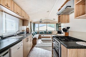 A compact RV kitchen with a stove, sink, and a dining area with a bench. - 3 Bed-Sleeps 8-Pet Friendly-Parking-Sea View (Exmouth)