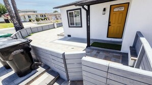 A residential area with a white house, a yellow door, and a black trash bin labeled "Property of the City of San Diego."