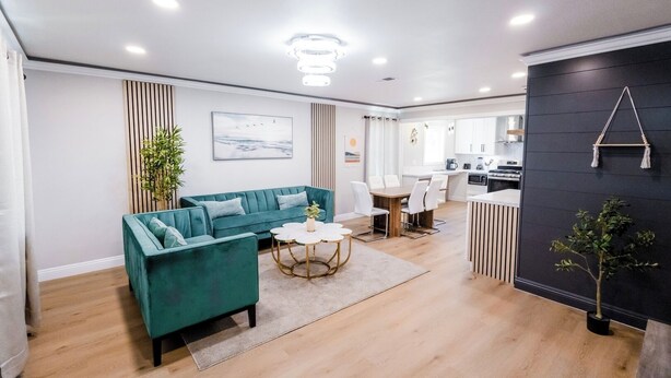 A modern living room with a teal sofa, a dining area, and a kitchen.