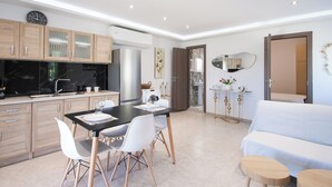 A modern kitchen with wooden cabinets, a dining table with chairs, and a sofa in a living area. - SkyFrame Apartments (Skiathos)