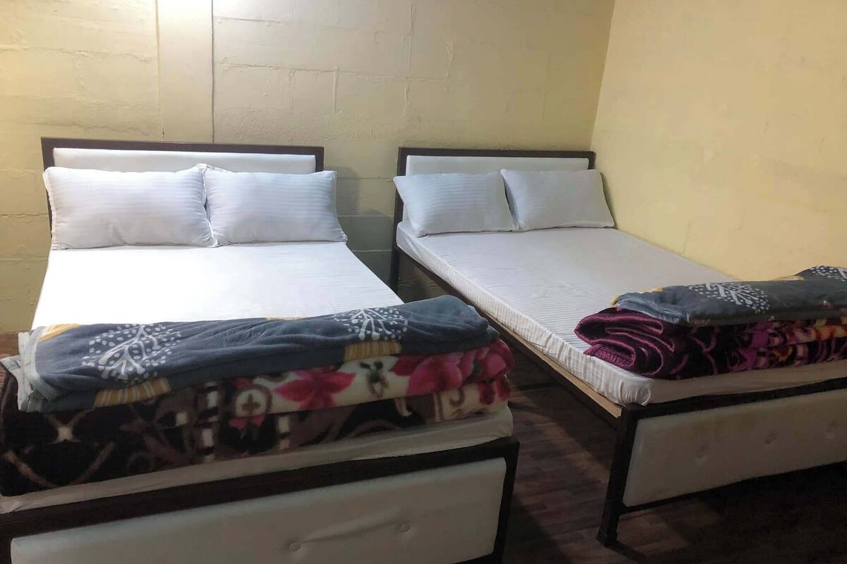 Two single beds with white linens and a lower bunk bed with a colorful blanket.