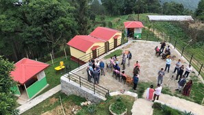 Um grupo de pessoas reunido em uma pequena área externa com um muro de pedra e um edifício com telhado vermelho.