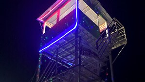 Estrutura metálica em torre com seção superior transparente e luzes LED coloridas.