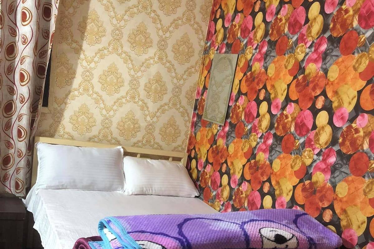 A bed with white linens, a floral-patterned wall, and a patterned curtain.