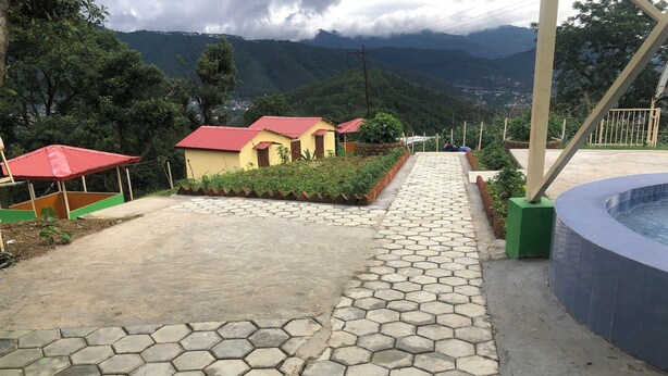 Uma trilha pavimentada conduz a um edifício com telhado vermelho, cercado por vegetação e montanhas ao fundo.
