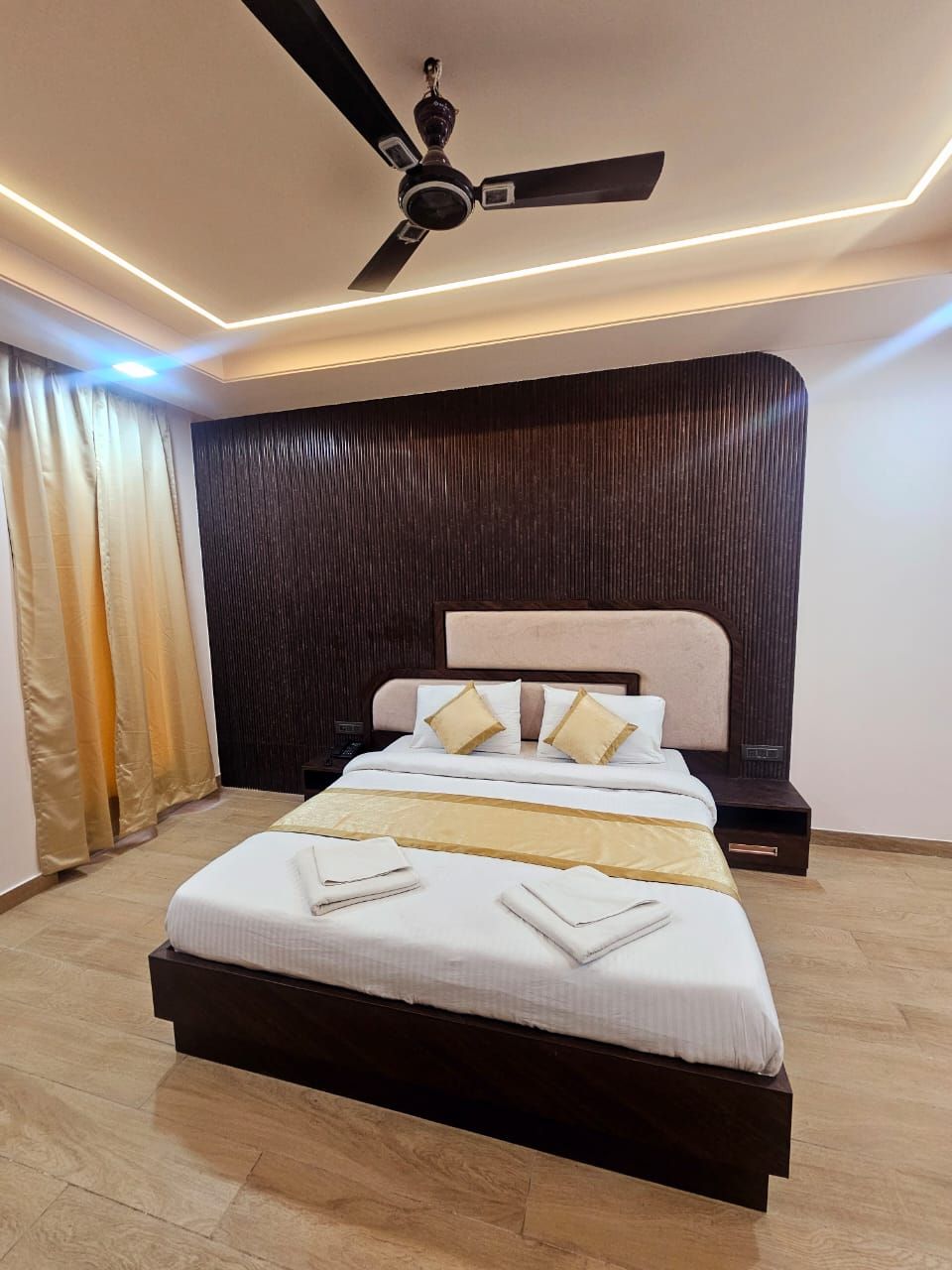 A modern bedroom with a large bed, a ceiling fan, and a dark wooden headboard.