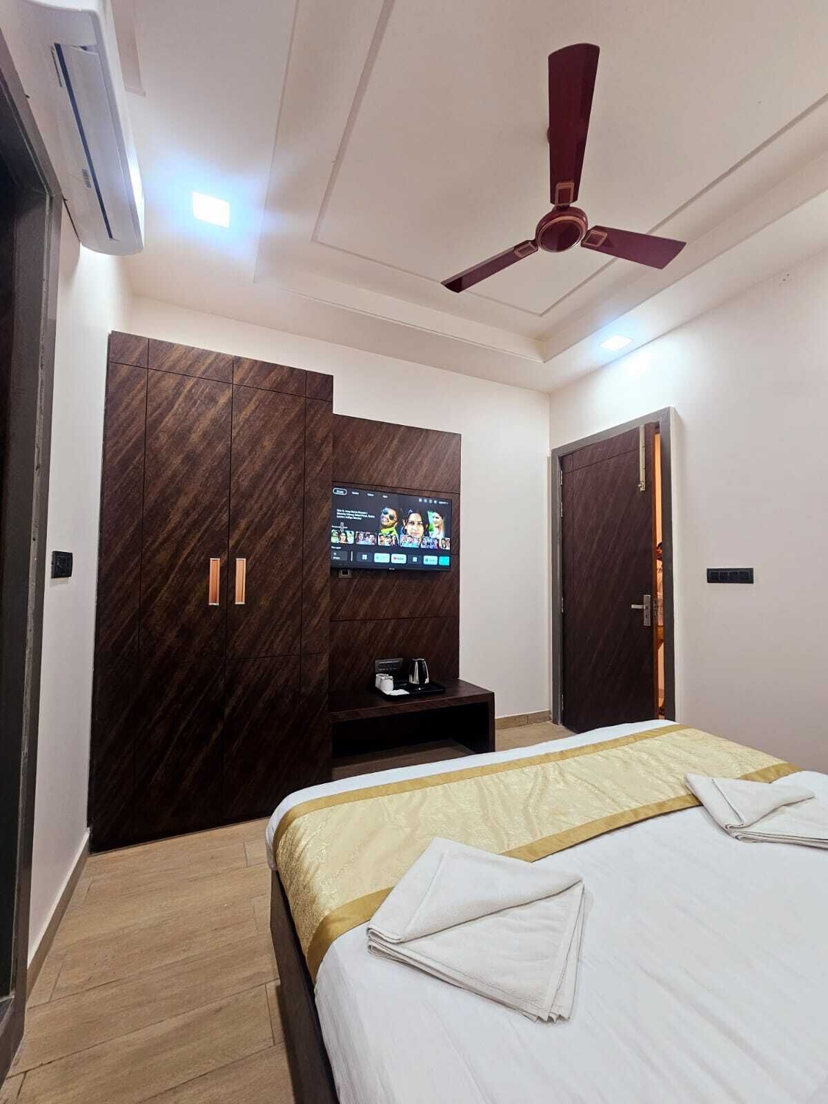Ein Hotelzimmer mit Bett, Wandfernseher, Kleiderschrank und Deckenventilator.