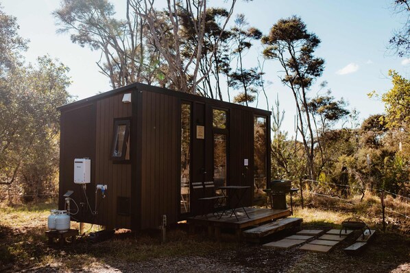 Una pequeña cabaña de madera con porche, panel solar y tanques de propano.
