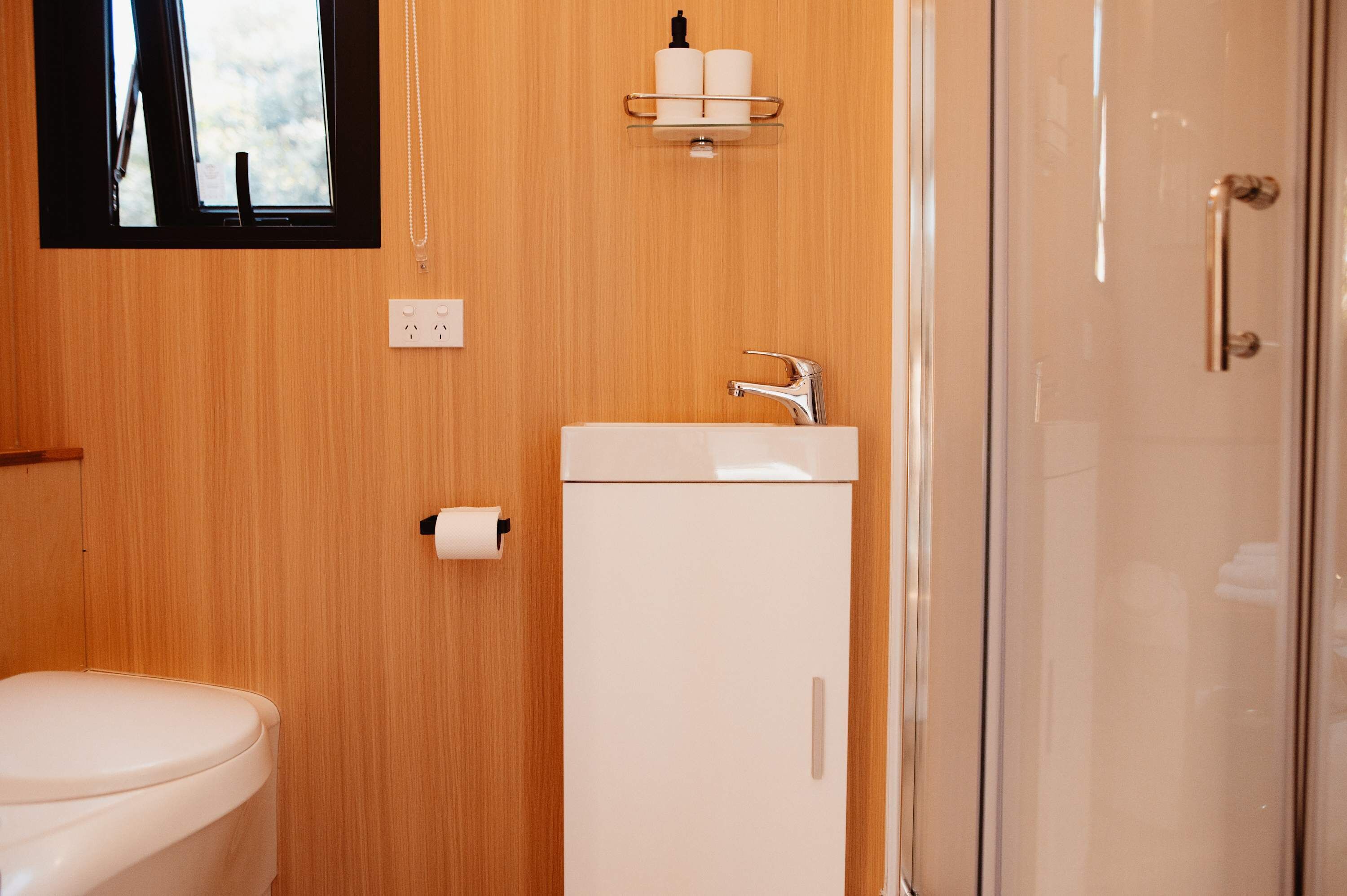 Et badeværelse med toilet, vask med hane, spejl og et vindue.