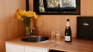 En köksbänk med en diskho i rostfritt stål, en vas med gula blommor, två champagneglas och en flaska champagne.