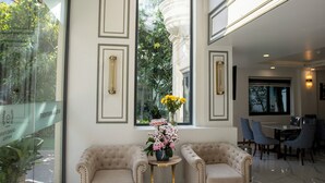 A spacious lobby with a high ceiling, a large arched window, and two plush armchairs facing a small table with a vase of flowers.
