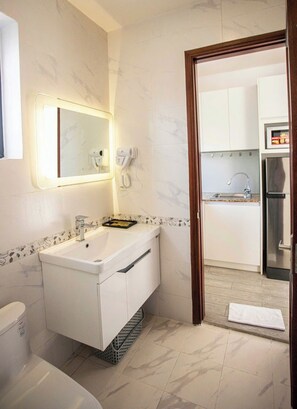 A modern bathroom with a white sink, a mirror with lights, a hairdryer, and a toilet. - Grand Park Hotel & Apartment Phu My Hung (Ho Chi Minh City)