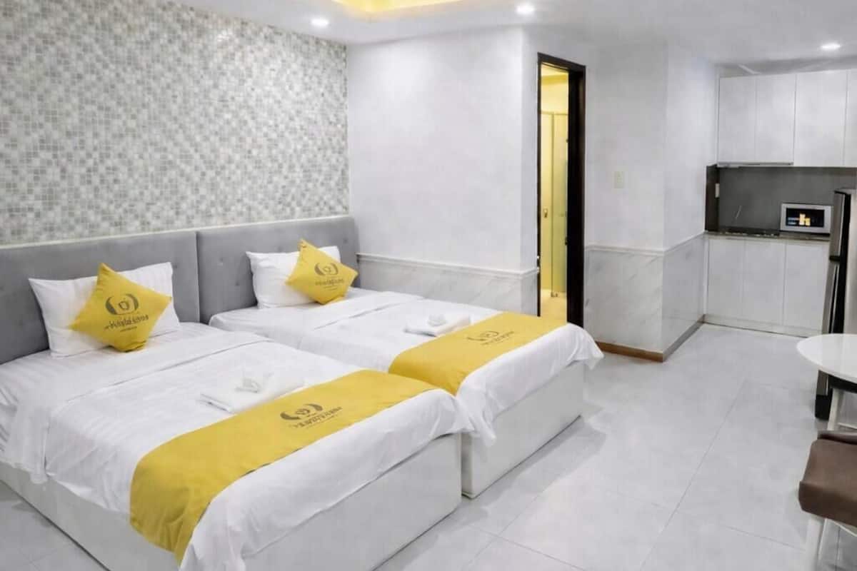 Quarto de hotel com duas camas, uma kitchenette pequena e um banheiro visível através de uma porta aberta.