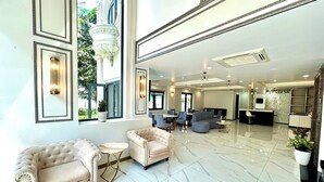 A spacious lobby with a marble floor, a seating area with two sofas, a reception desk, and a dining area.