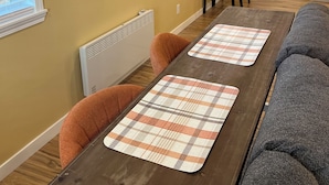A dining area with a wooden table, orange chairs, and a gray couch. A painting of surfboards is on the wall. - Sequim Getaway (Sequim)