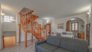 A spacious living area with a grey sofa, a wooden staircase, and a kitchen area with wooden cabinets and a window. - IL BORGHETTO - VILLINO IL BORGHETTO (Campo nell'Elba)