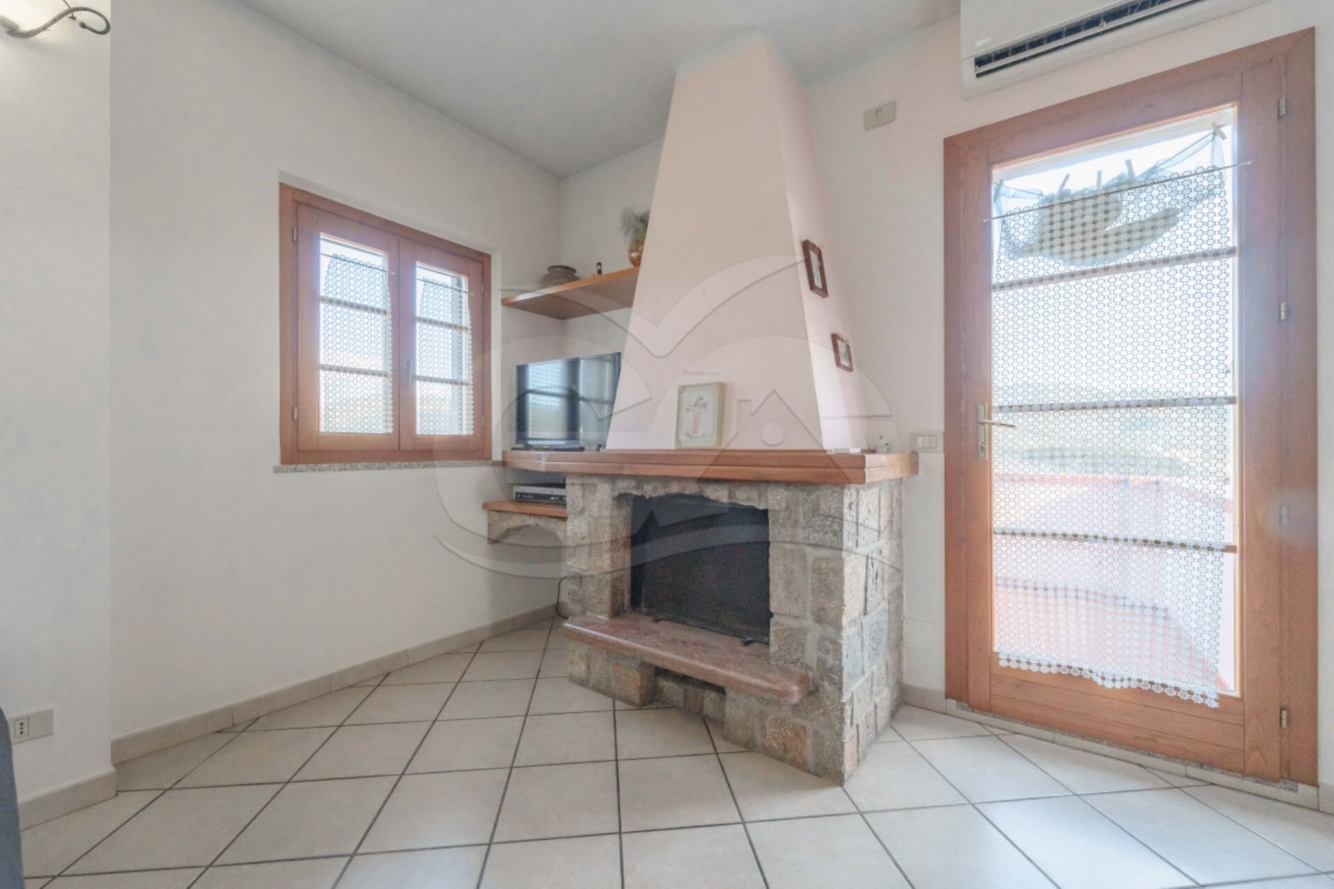 A living room with a stone fireplace, a television, and a window with a wooden frame.