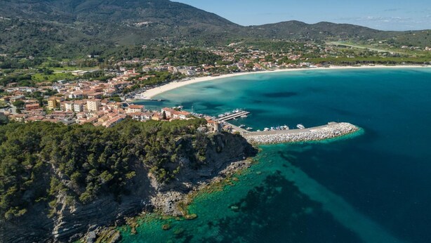 An aerial view of a coastal town with a beach, clear turquoise waters, and a rocky shoreline. - IL BORGHETTO - VILLINO IL BORGHETTO (Campo nell'Elba)