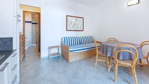A compact living space with a kitchenette, a dining area with a table and chairs, a striped sofa, and a small side table. - Appartamenti Arcipelago - Appartamenti Arcipelago - Bilocale (27) (Rio dell'Elba)