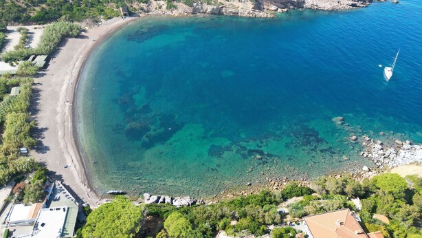 An aerial view of a coastal area with a clear blue sea, a sandy beach, and a small rocky outcrop. - Appartamenti Arcipelago - Appartamenti Arcipelago - Bilocale (27) (Rio dell'Elba)