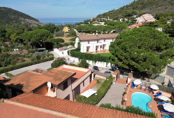 A residential area with a swimming pool, a white house with a red roof, and a view of the sea.