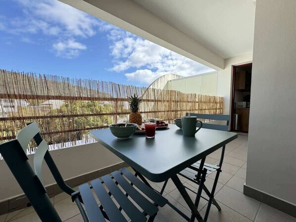 Un balcón con una mesa para dos, una silla y vistas al cielo y a los árboles.