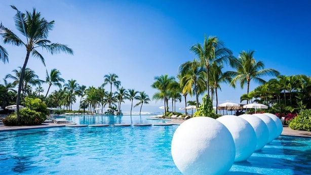 A resort pool with clear blue water, surrounded by palm trees and lounge chairs.