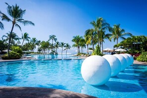 A resort pool with clear blue water, surrounded by palm trees and lounge chairs.
