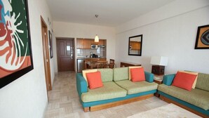 A living room with a sofa, a dining table, and a kitchen in the background.
