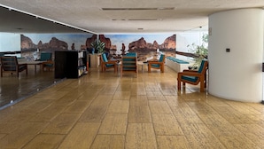 A spacious lobby with a large mural of a rocky coastline, wooden furniture, and a seating area with a view of the sea.