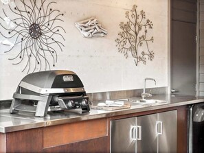 A kitchen with a built-in grill, stainless steel cabinets, and decorative wall art. - La Dimora—Tranquil Retreat Where Bush Meets Beach (Burnside)