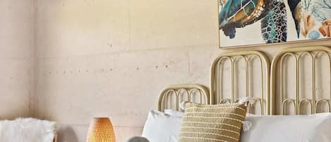 A neatly made bed with white linens and a rolled towel, a textured beige pillow, and a woven throw blanket.