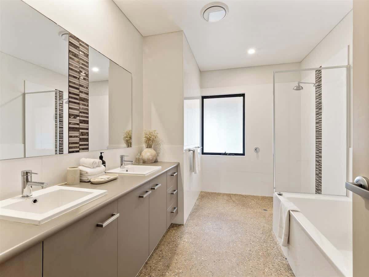 A modern bathroom with a large mirror, two sinks, a shower, and a window.