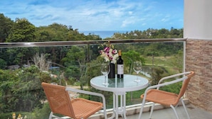 A balcony with two wicker chairs, a round glass table, and two wine bottles. - Tropical View Apartment Viva Patong A601 (Patong)
