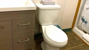 A bathroom with a white toilet, a wooden vanity with drawers, a white sink, and a shower curtain with a blue animal design. - The Tides Inn (Seward)
