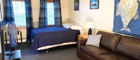 A hotel room with a bed, a brown leather sofa, a desk with a chair, and a ceiling fan.